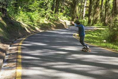 Man riding on a longboard skate on a road through a forest