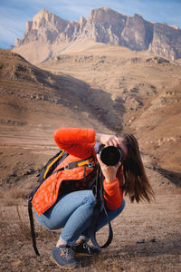 Young woman taking pictures while sitting on the background of mountains