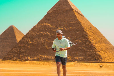 Full length of a man standing on sand at desert with the pyramids behind