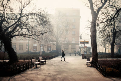 Side view of woman walking on footpath amidst bare trees