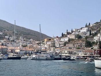 Sailboats moored in sea by townscape against sky