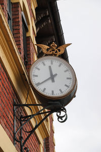 Low angle view of clock on wall against sky