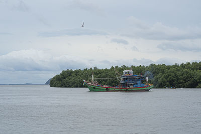 Langkawi island, malaysia - a single fishing boat going out to sea with an eagle flying overhead.