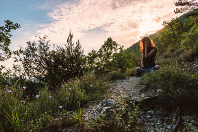 Woman sitting on rock against sky