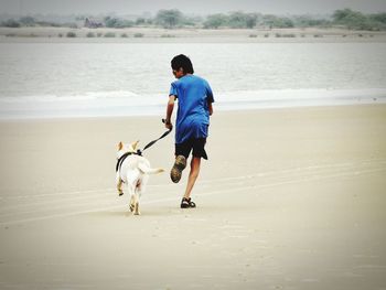 Full length of boy with dog running at beach