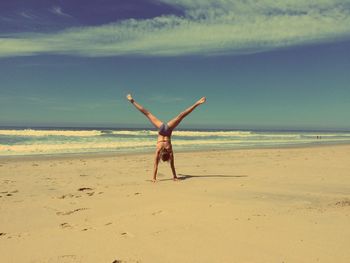 Woman doing handstand on beach against sky