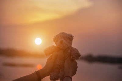 Hand holding toy against sky during sunset