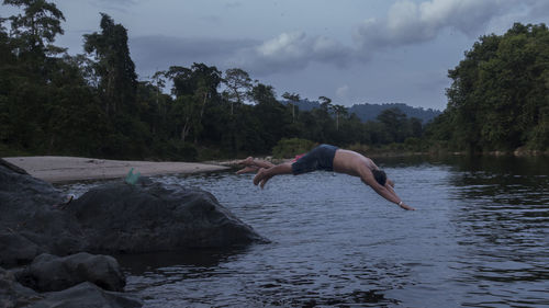 Shirtless male friends jumping in river at forest