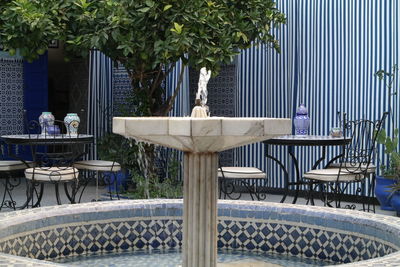 Chairs and table by fountain against trees