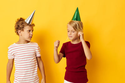 Portrait of smiling friends standing against yellow background