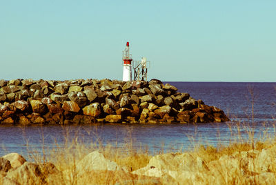 Lighthouse on rock by sea against clear sky