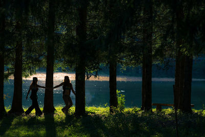 People standing by tree trunks in lake at forest