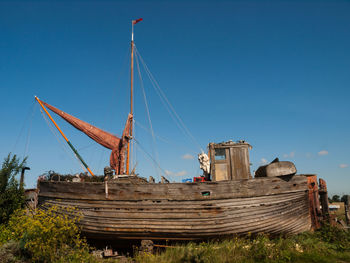 Abandoned boat on field against blue sky