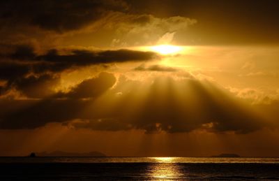 Sunlight streaming through clouds over sea during sunset