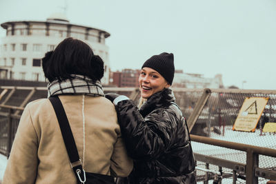 Portrait of cheerful young woman with friend standing on street in city during winter