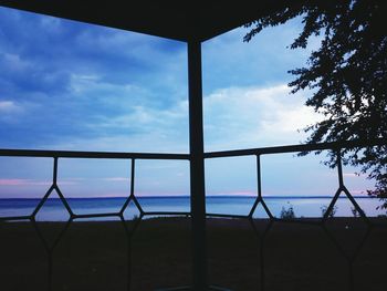 Silhouette railing by sea against sky