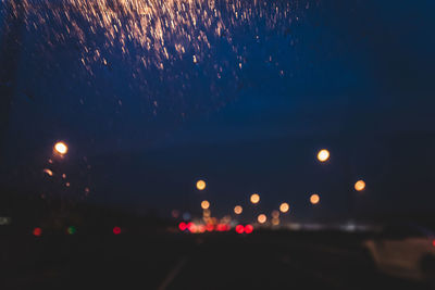 Road against sky at night seen through wet car windshield during rainy season