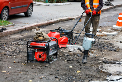 A road worker wearing a reflective orange vest repairs, installs sewers using compactor,  jackhammer