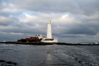 Lighthouse at beach against cloudy sky