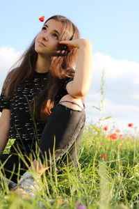 Young woman looking away on field against sky