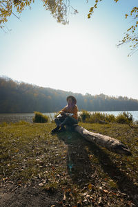 Rear view of woman sitting on field against sky
