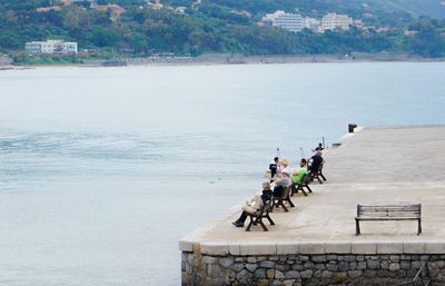 High angle view of people sitting on benches at pier in sea