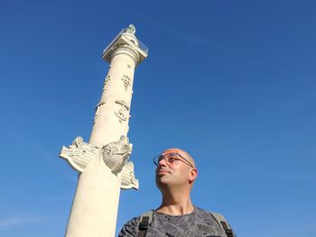 Low angle view of mid adult man looking away while standing against blue sky during sunny day
