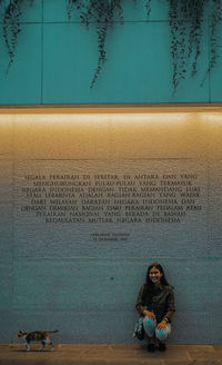 Full length portrait of woman sitting against wall against building