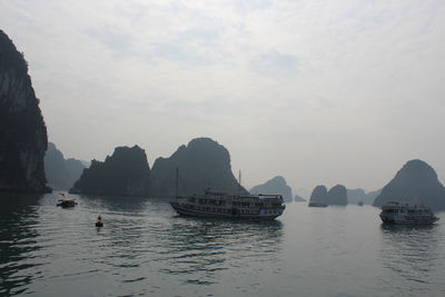 Boats on halong bay by rock formations against clear sky