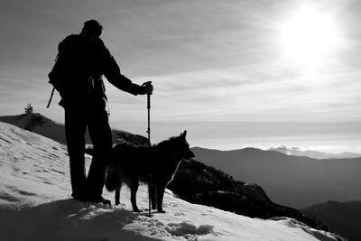 Silhouette man with dog standing on snowcapped mountain against sky