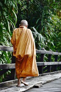 Rear view of monk walking on wooden footbridge against trees