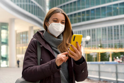 Woman with winter clothes typing finger chatting with someone on smartphone wearing protective mask