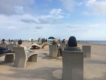 People sitting on beach by sea against sky