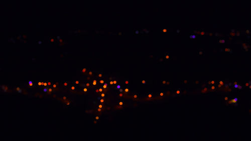 Defocused image of illuminated lights against sky at night