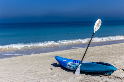 Kayak and oar on beach against blue sky