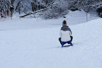 Rear view of woman crouching on snow covered land