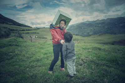 Mother wearing mirror while standing by son on grassy field