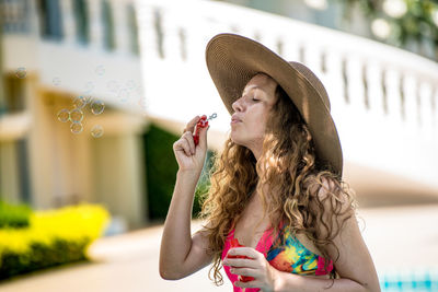 Woman wearing hat blowing bubbles in city