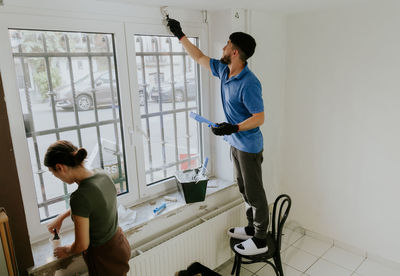 A young oriental couple paints a window opening with a brush.