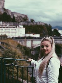 Portrait of smiling young woman standing against railing