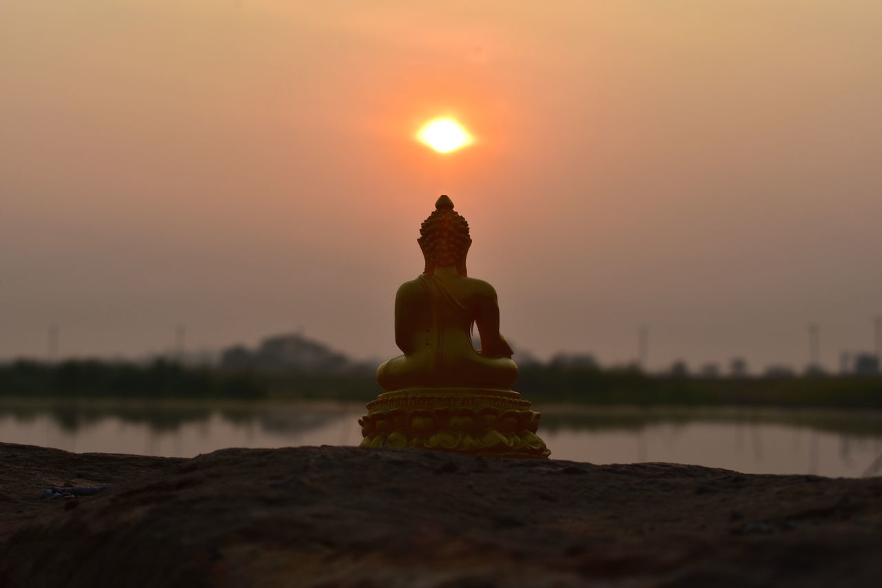 STATUE OF BUDDHA AGAINST ORANGE SKY