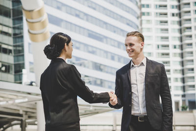 Business people giving handshake while standing against building in city