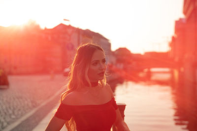 Portrait of young woman against lake during sunset