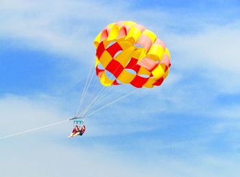Low angle view of women parasailing against sky