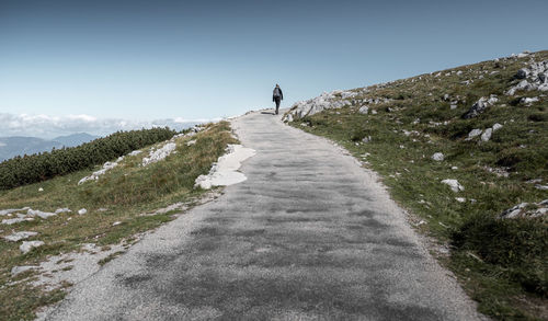 Rear view of woman walking on road on hill against sky