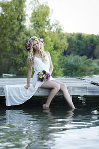 Woman with flowers sitting on jetty over lake against trees