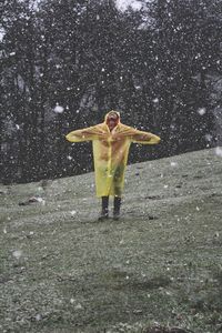 Young man with arms outstretched standing in snowfall