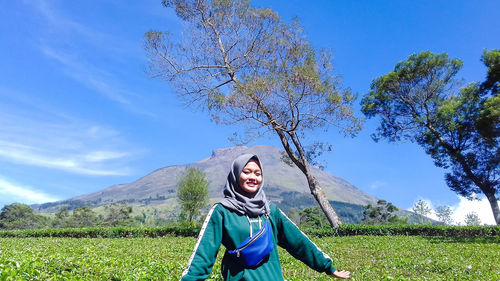 Young woman with arms raised on field against sky