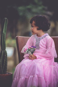 Rear view of woman holding pink while sitting on plant