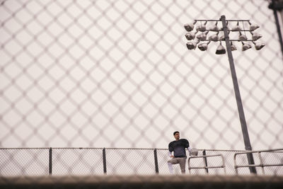 Low angle view of american football player looking away while standing in stadium seen through fence